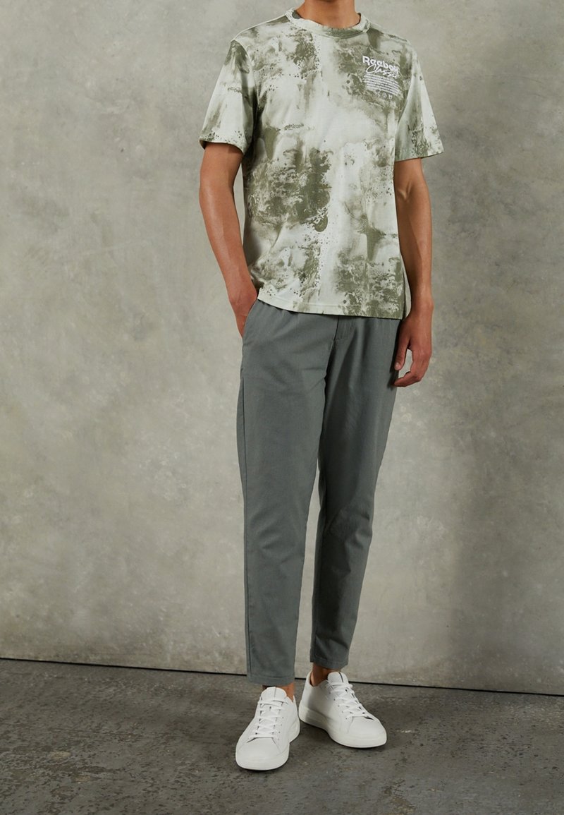 Svetle zelená košile s krátkým rukávem s mramorovým vzorem a logem; spárováno s šedými zúženými kalhotami a bílými teniskami.