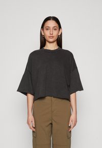 Tamno sivi oversize T-shirt s okruglim izrezom i kratkim rukavima, koji ima ležeran kroj i mekani, teksturirani materijal.