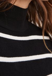 Zwarte geribbelde trui met een hoge nek, voorzien van witte horizontale strepen. Close-up weergave benadrukt de textuur en de plaatsing van de strepen.