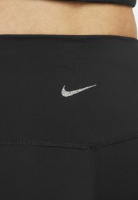 Czarne legginsy sportowe wykonane z gładkiego materiału, z małym, iryzującym logo Nike na pasku i precyzyjnymi detalami szycia.