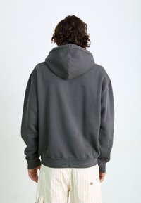 Hanorac gri cu glugă, cu o croială lejeră, având o margine și mansete ribbate. Prezintă o textură netedă, fără elemente decorative, și un design minimalist.