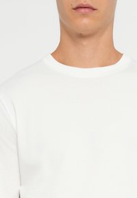 T-shirt bianco a maniche corte in cotone con scollatura rotonda, texture liscia e design minimalista; si concentra su linee pulite e semplicità.