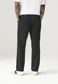 Zwarte broek met een recht model, gemaakt van geweven stof. Voorzien van een achterzak, in combinatie met witte schoenen versierd met een zwarte band.