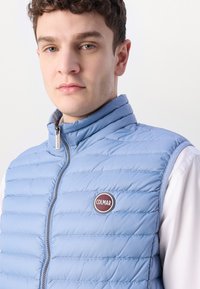 Svijetloplava выполнить дносна вест с високом ovratnikom, с zatvaračem, i округлим Colmar logom s prednje strane. Glatka tekstura s pojednostavljenim dizajnom.