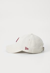 Casquette beige clair avec une visière incurvée, logo bordeaux brodé à l'avant et sangle ajustable à l'arrière. Finition en tissu texturé.
