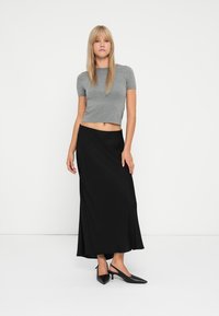 T-shirt gris court associé à une jupe midi noire fluide. La tenue présente une texture lisse et des chaussures à stilettos noires élégantes.