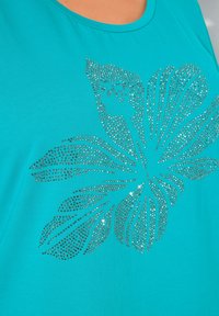 Camiseta turquesa con un diseño floral hecho de brillantes strass plateados, con un cuello redondo y textura suave.