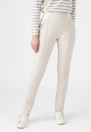 Persona che indossa pantaloni beige chiaro aderenti con cuciture verticali, una camicia a righe a maniche lunghe e sneakers bianche con lacci.
