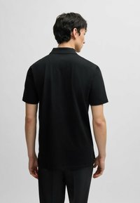 Polo shirt nero a maniche corte con colletto polo e orlo dritto. Realizzato in tessuto morbido, presenta cuciture minimali e una texture liscia.