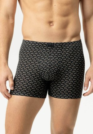 Männlicher Torso trägt schwarze Boxershorts mit einem sich wiederholenden Muster kleiner beiger laufender Pferde auf hellem Hintergrund.