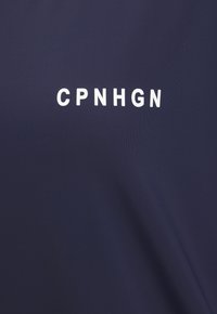 Jūras zilas krāsas audums ar gludu tekstūru, kurā centrā izcili ir iespiesti baltie burti "CPNHGN".