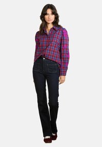 Kostkovaná košile s fialovými a růžovými tóny, má dlouhé rukávy a detailní výšivku; kombinována s tmavě modrými zvonovými džíny a burgundskými botami.