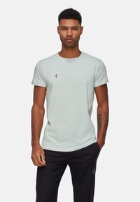 T-shirt vert clair à manches courtes en tissu doux, arborant un petit logo coloré brodé sur la poitrine, avec un col rond.