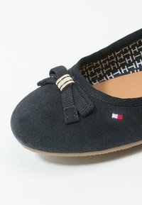 Ballerines en suède noir avec un nœud et des anneaux dorés sur le bout, semelle intérieure beige et doublure intérieure à motif de lettres "H".
