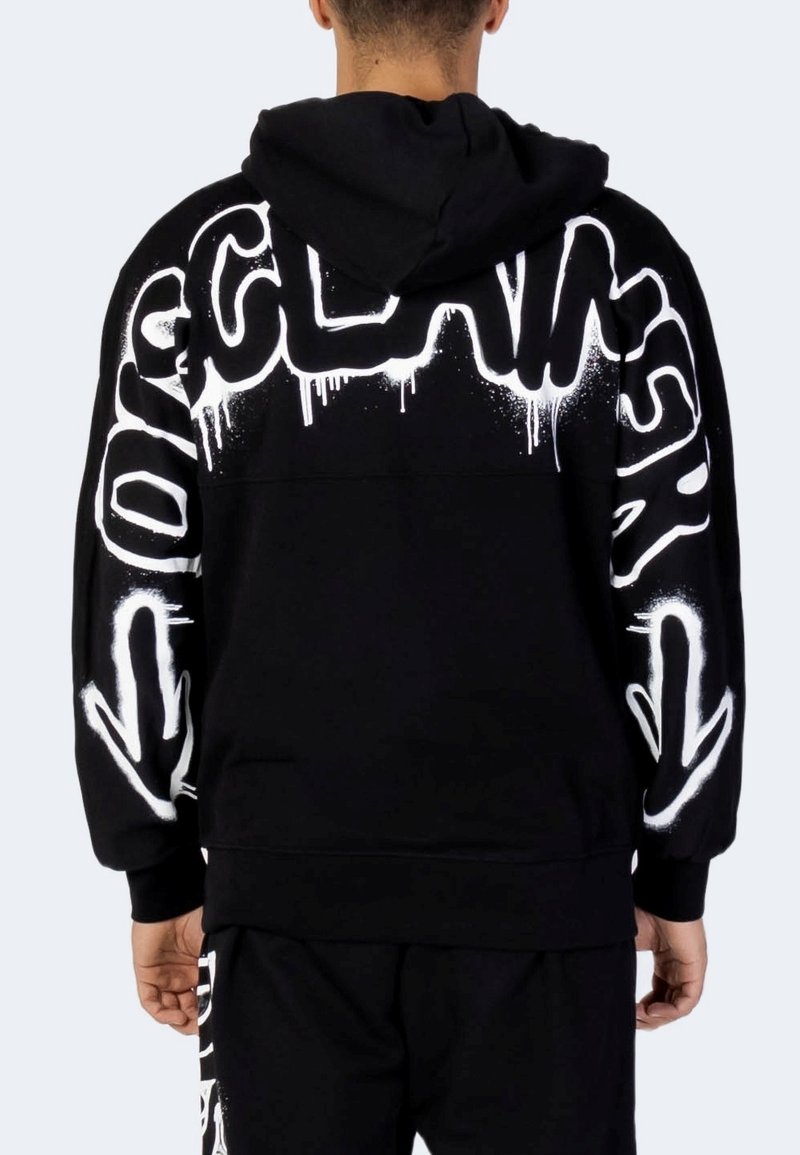 Persona che indossa un felpa nera con testo in stile graffiti bianco e frecce sulla schiena e sulle maniche, abbinata a pantaloni neri coordinati.