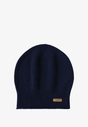 Hellrosa Wollmantel mit Bindegürtel, zwei Vorderentaschen, kombiniert mit einem dunkelblauen Schal und einer Mütze; das Modell trägt hellblaue, verwaschene Jeans und schwarze Schuhe.