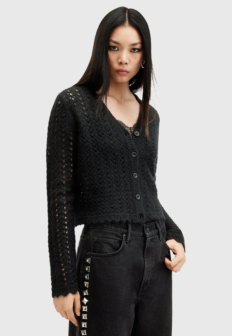 Svart stickad cardigan med v-ringning, knappstängning, strukturerad mönster och vågig fåll. Kombinerad med högmidjade svarta jeans med nitar.