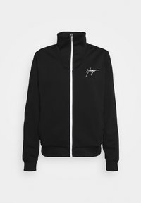 Sudadera negra con cremallera fabricada en tejido suave. Presenta un cuello alto, una cinta de cremallera blanca y el logotipo blanco "Hugo" en el lado izquierdo del pecho.