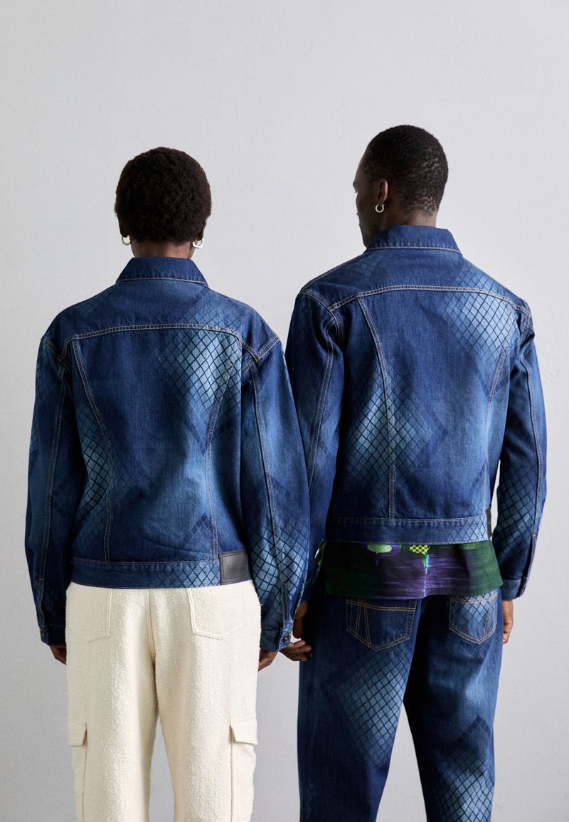 Jeansjacks met een ruitenpatroon, donkerblauwe wassing en contrasterende lichtblauwe accenten op de schouders. Gecombineerd met beige textuurbroeken.