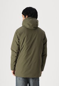 Olive green waterproof jacket with a hood, features a smooth texture, long sleeves, and loose fit. Visible stitching and no notable patterns.