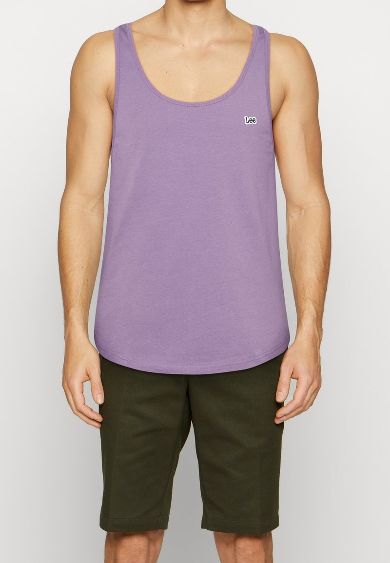 Débardeur violet en coton, avec un col rond et un petit logo brodé. Associé à un short vert foncé arrivant aux genoux.