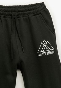Zwarte trainingsbroek met een trekkoord in de taille, zijzakken en een wit "LIMITED EDITION" logo met overlappende berggrafieken.