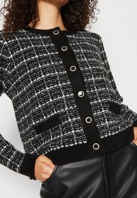 Cardigan a righe bianche e nere con bottoni metallici rotondi, tessuto testurizzato, polsini a costine e due tasche frontali.