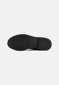 Semelle de botte en caoutchouc noir avec un motif de semelle texturé, des rainures profondes et un talon renforcé, conçue pour l'adhérence et la durabilité.
