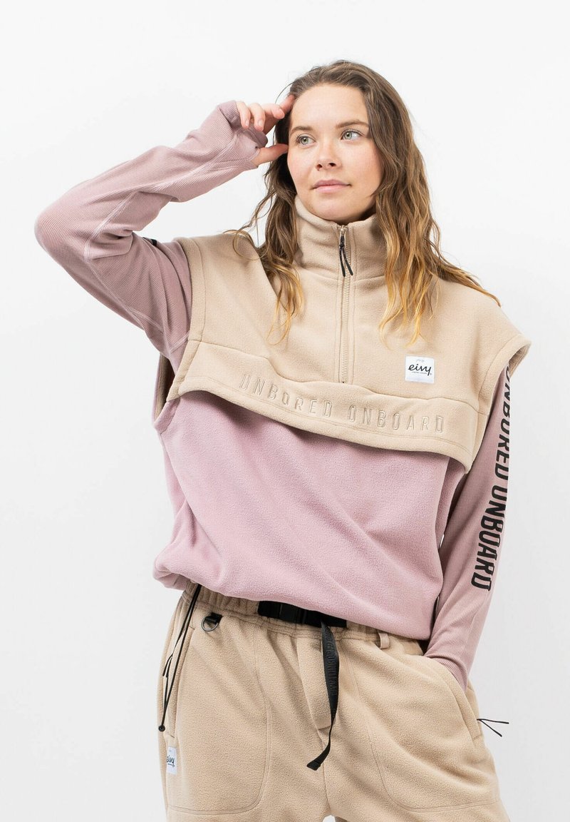 Fleece-Pullover mit hohem Kragen, in einem beigen Oberteil und einem pinken Unterteil. Auffälliger Text "UNBORED ONBOARD" auf der Brust.