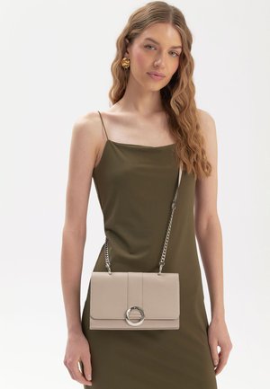 Borsa a mano in pelle sintetica beige con un accento circolare argentato e una tracolla a catena, forma rettangolare, texture liscia e design minimalista.