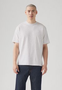 Light gray short-sleeve t-shirt with a subtle textured pattern and a small logo on the chest, paired with dark denim jeans.