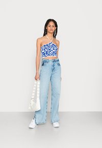 Top cropped azul e branco com padrão e decote halter, combinado com jeans de perna larga azul clara e uma bolsa branca com detalhes de tachas.