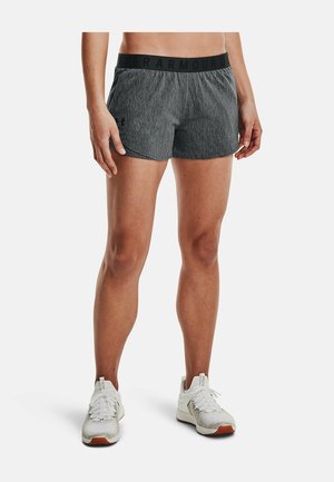 Atleta con pantalones cortos Under Armour grises texturizados y zapatos deportivos blancos, de pie sobre un fondo blanco liso.