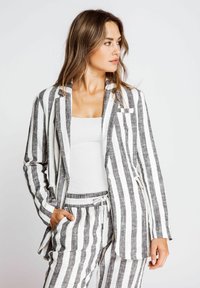 Striped linen blazer in black and white, featuring an open front, single chest pocket, and relaxed fit, paired with matching striped pants.
