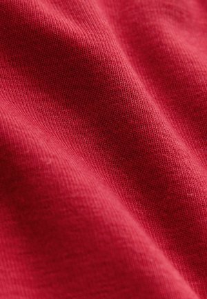 Červená bavlnená látka s rebrovanou textúrou, ktorá obsahuje jemné odtiene a prepletané detaily, vytvárajúce mäkký a textúrovaný vzhľad.