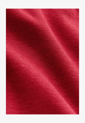 Röd bomullstyg med en räfflad struktur, med subtila nyansvariationer och invävda detaljer som skapar ett mjukt och texturerat utseende.