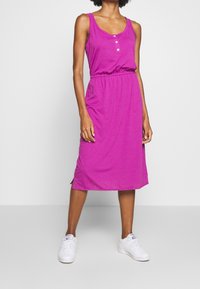 Robe fuchsia sans manches avec un col rond, avec des boutons à l'avant et une taille élastique, arrivant au milieu du mollet avec des fentes latérales.