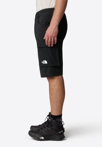 Black cargo shorts with multiple pockets, a fitted design, and a logo on the leg, paired with black hiking shoes.