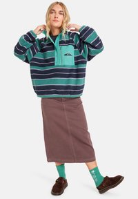 Fleece pulover s tirkiznim i tamnoplavim prugama, dizajn s polu-zipom, prednji džep, u paru s smešnim suknjom i šarenim zelenim čarapama.