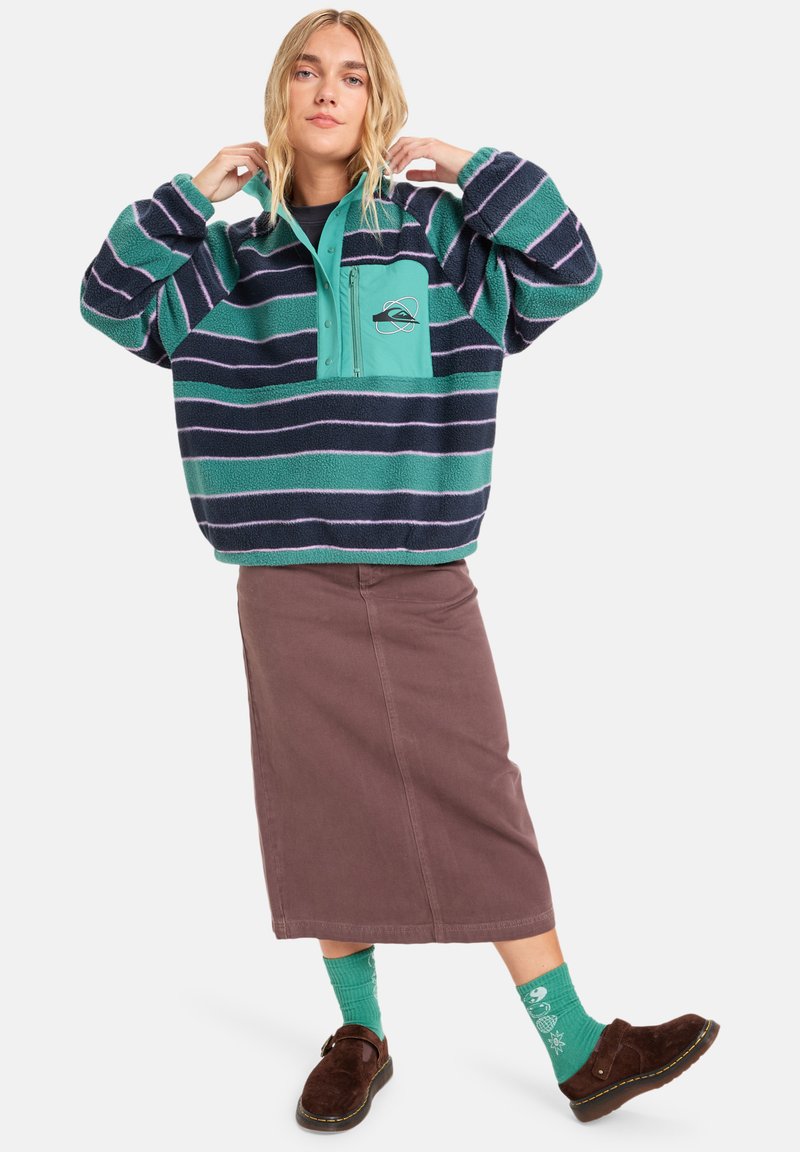 Fleece pulover s tirkiznim i tamnoplavim prugama, dizajn s polu-zipom, prednji džep, u paru s smešnim suknjom i šarenim zelenim čarapama.