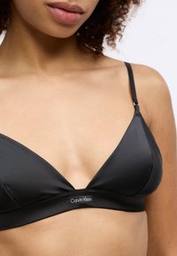 Bralette triangulaire noire en tissu lisse, dotée d'un bandeau logo et de bretelles réglables. Design minimaliste avec un décolleté en V.