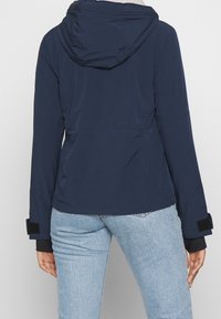 Námořnická bunda s kapucí a hladkým povrchem, elastickými manžetami a nastavitelné přizpůsobení v oblasti pasu. Materiál je lehký, bez viditelných vzorů.