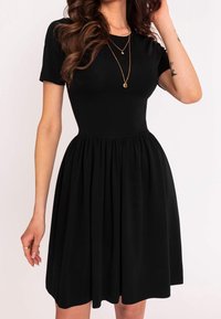 Vestido negro de manga corta con un corpete ajustado y una falda acampanada y plisada. Hecho de una tela suave, cuenta con un escote redondo y una textura en capas.