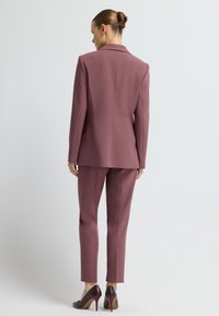 Mauve pak met gestructureerde blazer en slim-fit broek, gladde stoftextuur en minimalistisch ontwerp. Hakken complementeren de outfit.
