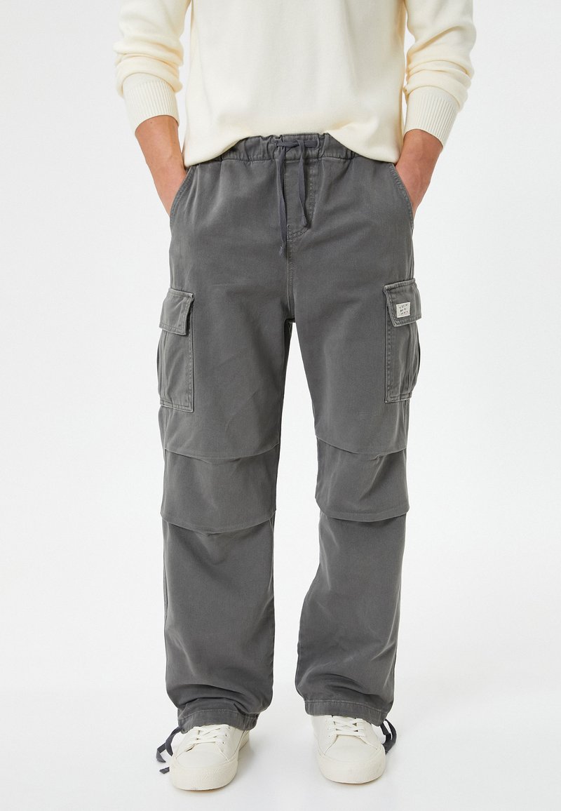 Pantalones cargo grises con una cinturilla elástica, cordón, múltiples bolsillos laterales y un ajuste holgado, hechos de un tejido duradero.