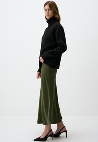 Zwarte coltrui, comfortabele pasvorm, gecombineerd met een groene satijnen maxi rok, met een gladde textuur en een vloeiende silhouet. Zwarte hoge hakken.
