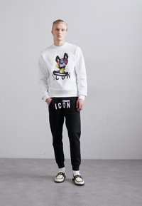White sweatshirt with colorful graphic depicting a dog and text "ICON." Black tapered pants with "ICON" and logo details. Casual footwear.