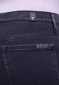 Donkerdenim jeans met een zichtbaar label met het nummer "7" en een merklabel op de achterzak. Bevat standaard stiksels en een gestructureerde stof.