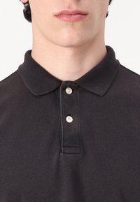 Svart polo-skjorte med teksturert stoff, to hvite knapper og klassisk kragedesign. Egnet for uformell eller semi-formell bruk.