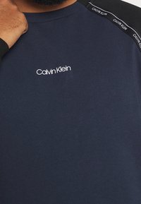 Camiseta azul marino de Calvin Klein con textura acanalada, que presenta un logo blanco en el pecho y detalles de tela negra en los hombros.